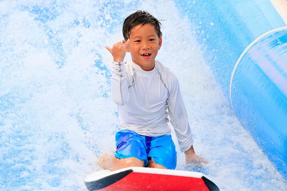 Young boy playing in water slide at resort with splashing water and blue background