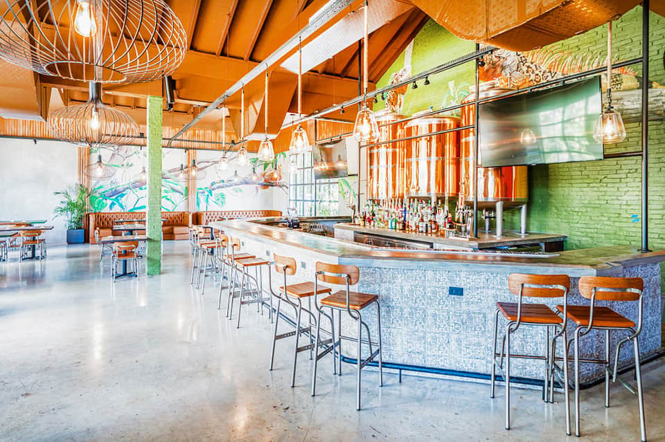 Modern bar lounge with orange pendant lights, green brick walls, and wooden bar stools