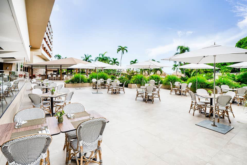 Modern rooftop terrace with white umbrellas, rattan chairs, and tropical landscaping