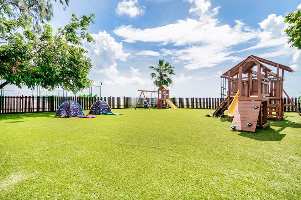 Children's playground with play tent, wooden structure, and swings on manicured green lawn