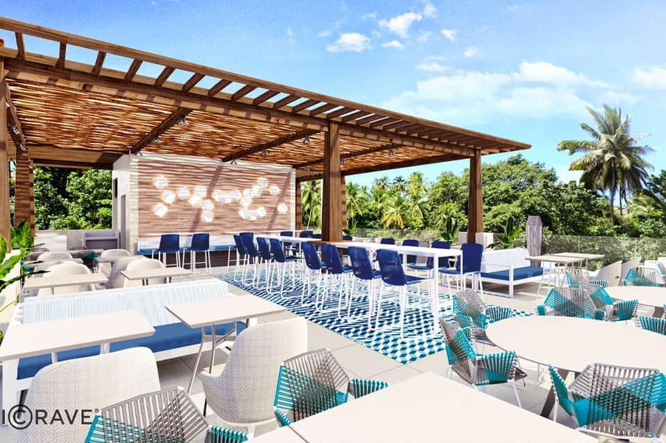 Modern outdoor lounge with wooden pergola, blue and white seating, geometric patterned rug, and tropical views
