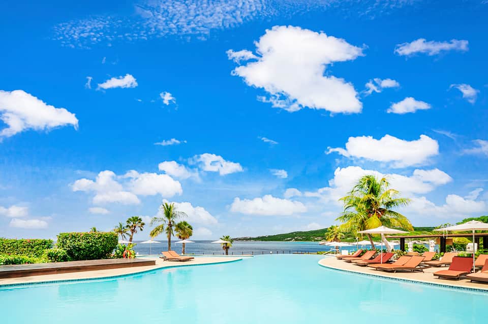 Oceanfront resort pool with lounge chairs, palm trees, and clear blue sky