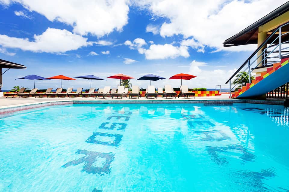 Bright blue resort swimming pool with lane markers and umbrellas, surrounded by lounge chairs