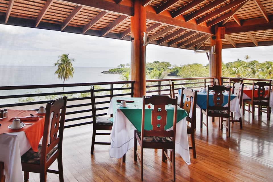 Oceanview restaurant with wooden pavilion, colorful tablecloths, and palm trees