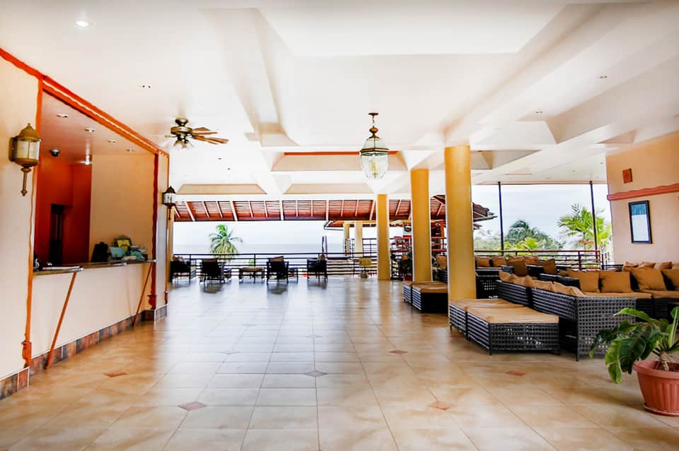 Resort lobby with terra cotta accents, white columns, ceiling fans, and ocean view balcony
