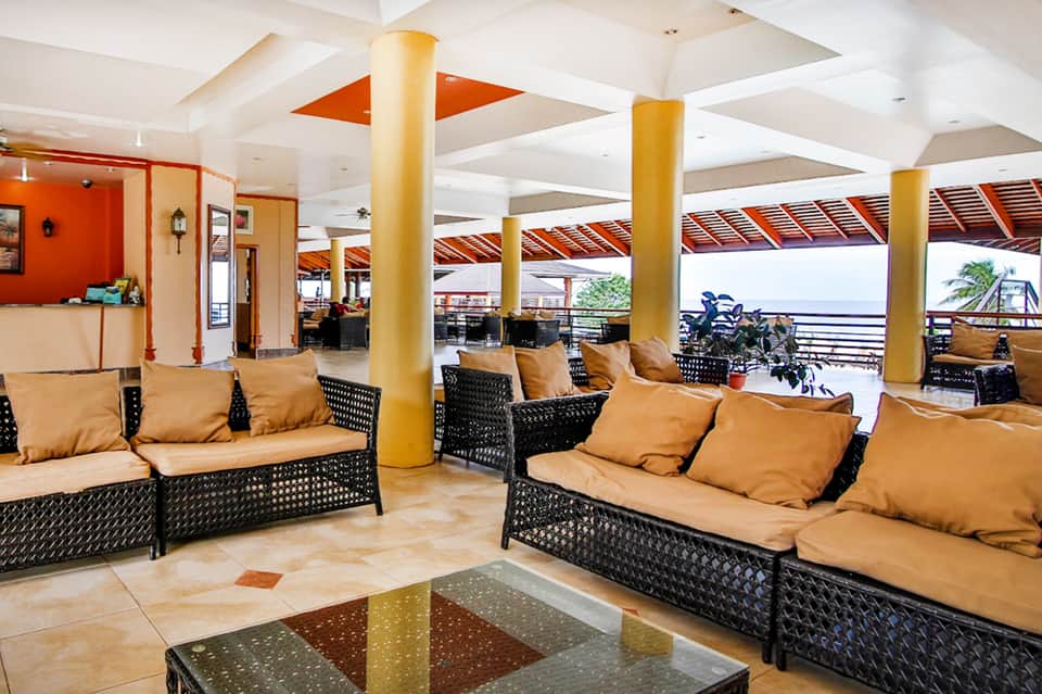 Resort lounge with black wicker seating, tan cushions, yellow columns, and ocean view