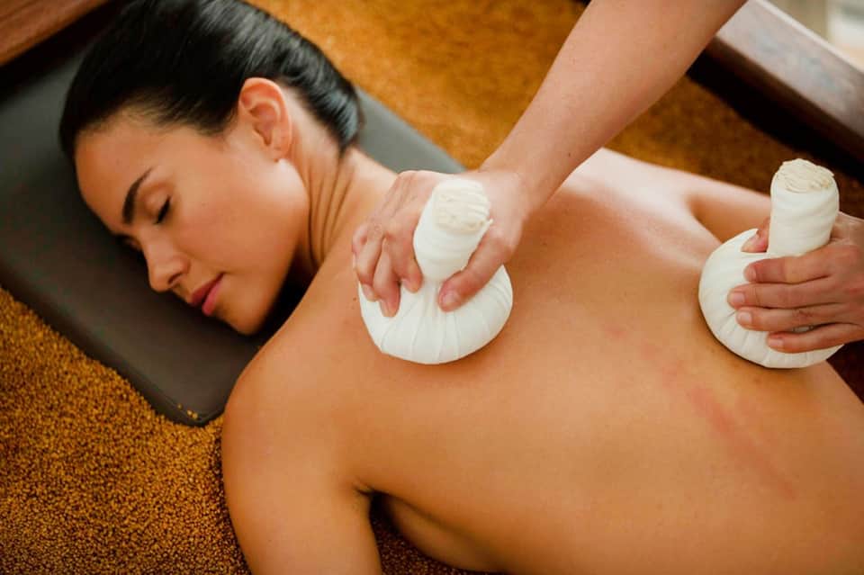 Spa therapist applying warm herbal compress treatment to client's back