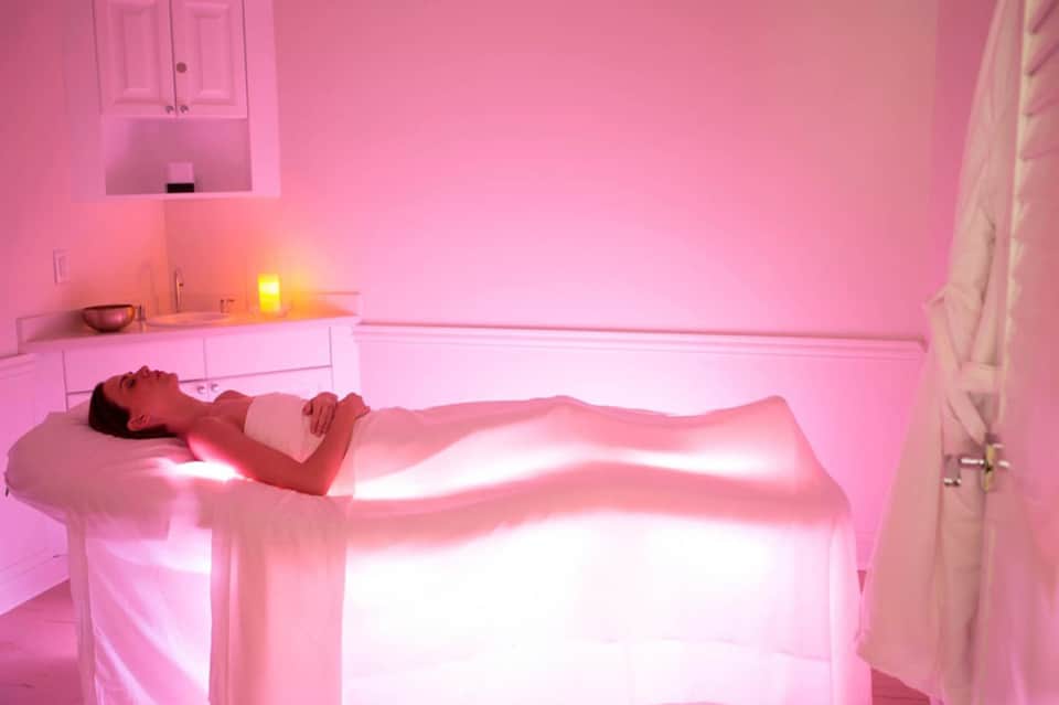 Person undergoing infrared light therapy treatment in pink-lit wellness spa room with minimalist design