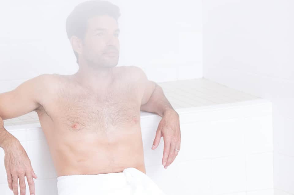 Shirtless man relaxing on white chair against minimalist white background