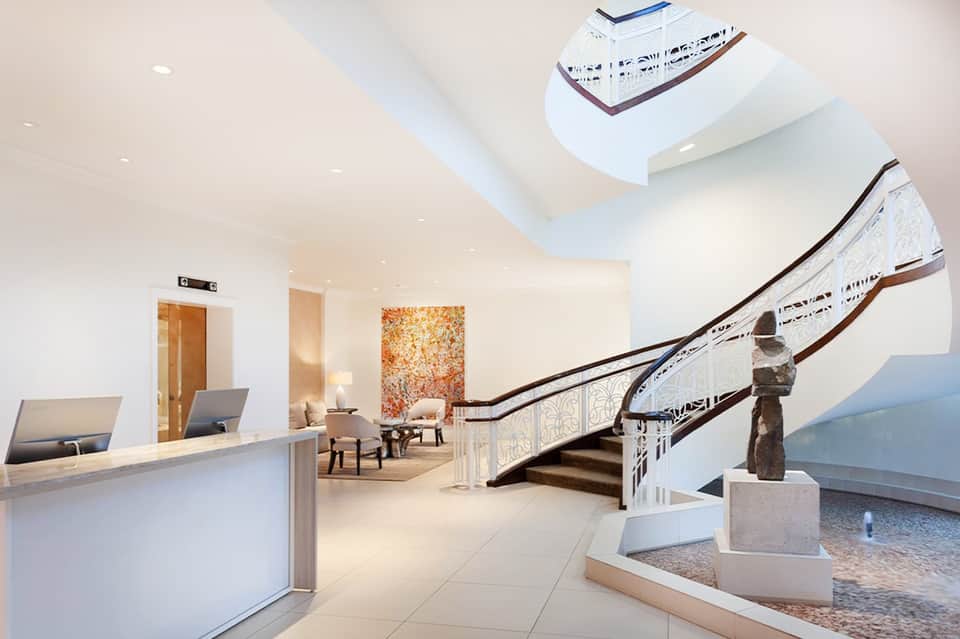 Modern cruise ship lobby with grand staircase, skylight, and reception desk