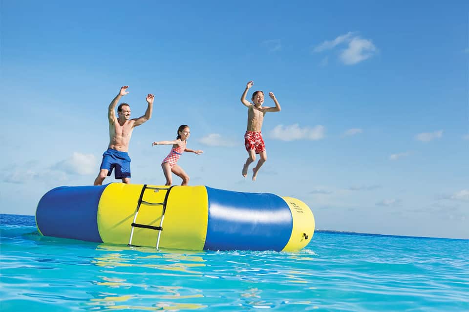 Four children jumping on yellow and blue inflatable water trampoline in ocean
