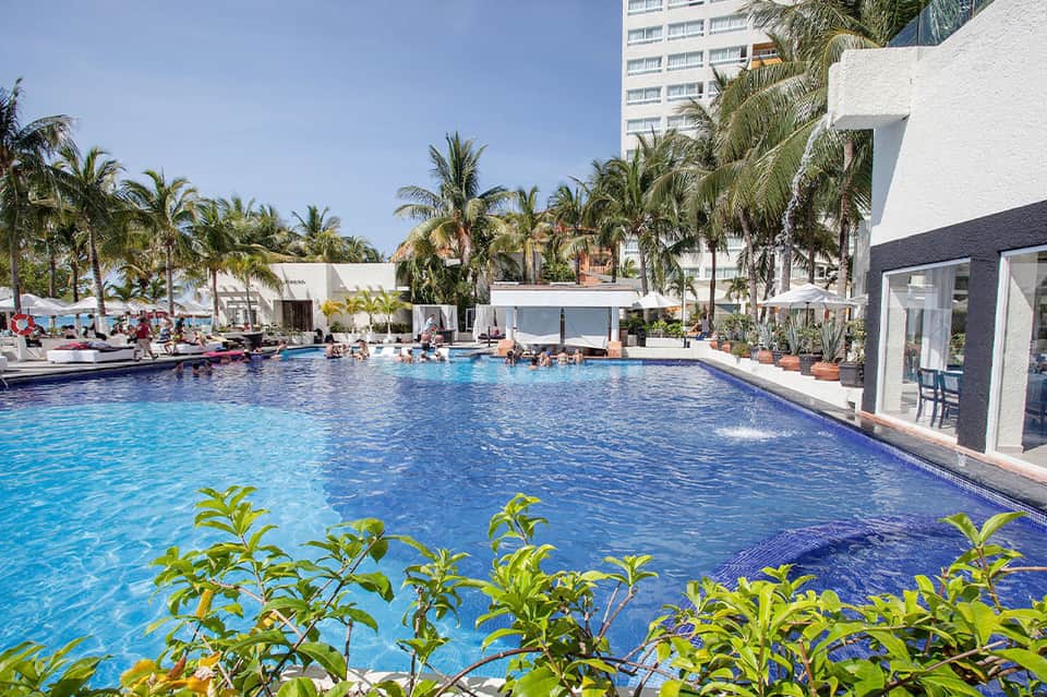 Resort swimming pool surrounded by palm trees with white cabanas and loungers
