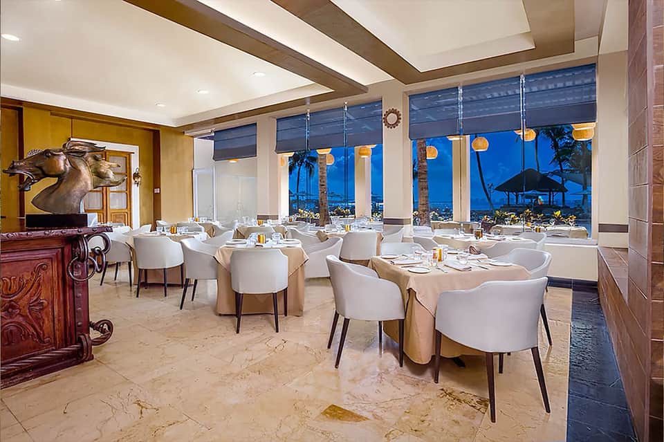 Upscale beachfront dining room with white chairs, ocean views, and elegant evening setting