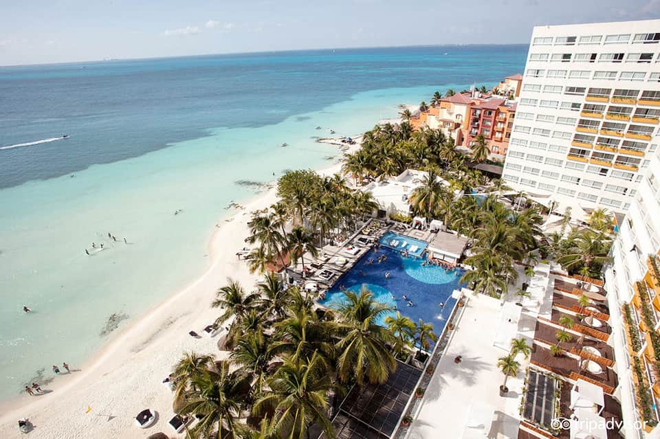 Aerial view of beachfront resort with blue pool, sandy beach, and turquoise ocean water