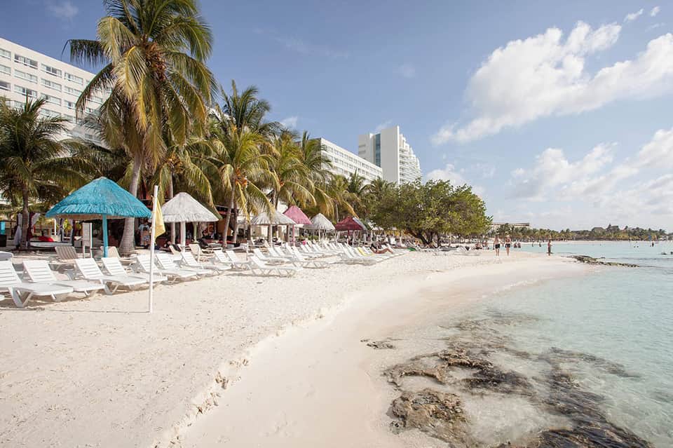 Beach resort with white loungers, colorful umbrellas, palm trees, and calm turquoise water