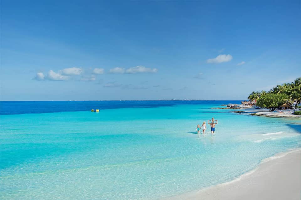 Guests wading in crystal-clear turquoise ocean water on pristine white sand beach