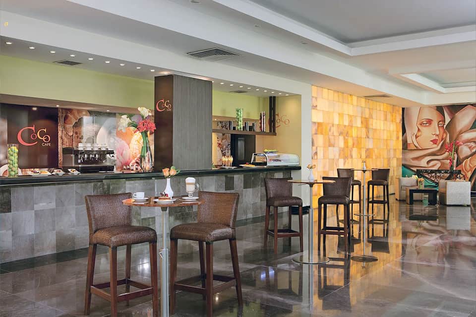 Modern café interior with yellow walls, neon sign, counter seating, and artistic wall murals