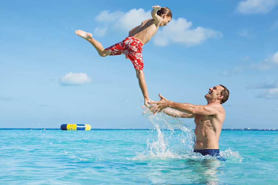 Father and child playing in turquoise ocean water with blue floatie device