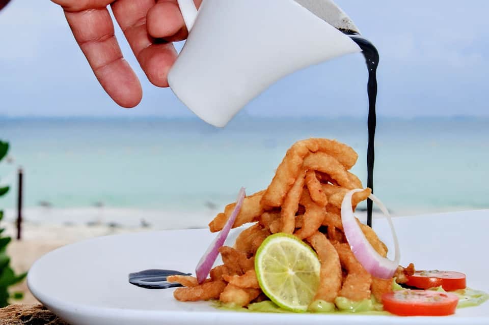 Gourmet fried shrimp dish with lime and black sauce on beach backdrop with ocean view