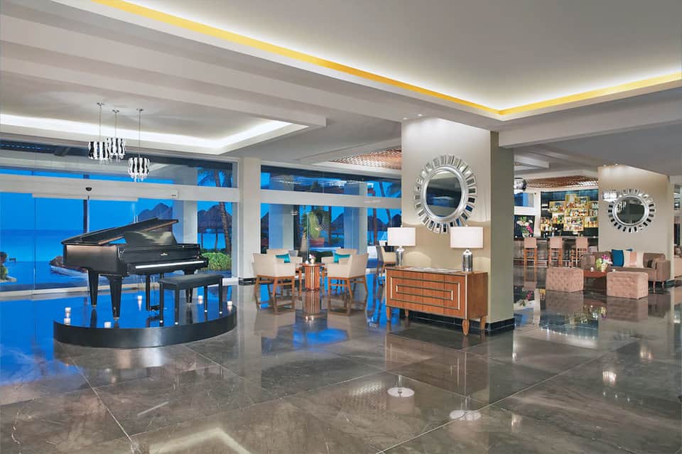 Luxury hotel lobby with grand piano, modern lighting, fireplace, comfortable seating, and ocean views