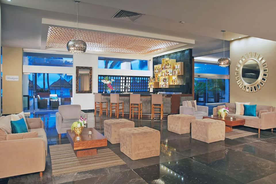 Upscale hotel lounge with geometric ceiling, bar seating, elegant furnishings, and floor-to-ceiling windows