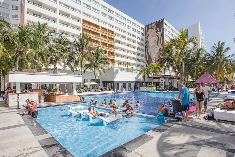 Active resort pool with families enjoying shallow water, tropical high-rise towers, and beachfront atmosphere