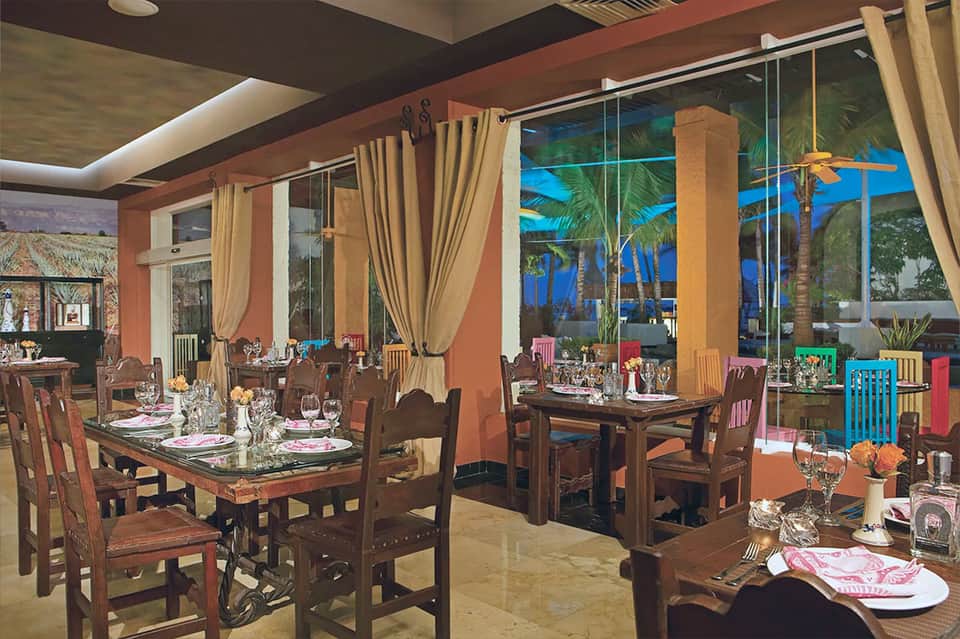 Elegant beachfront dining room with floor-to-ceiling windows, wooden tables, and ocean sunset views