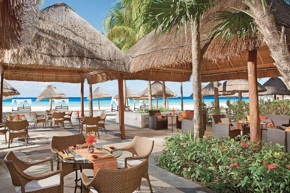 Beachfront restaurant with thatched umbrellas, woven chairs, and ocean views