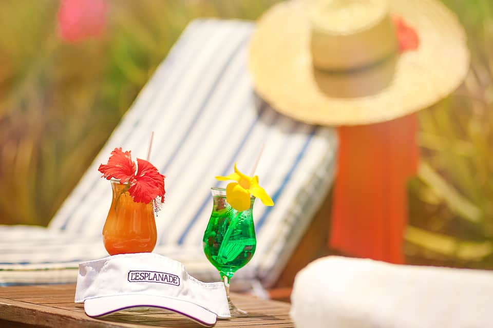 Tropical drinks with flower garnishes on wooden table with guest in sun hat