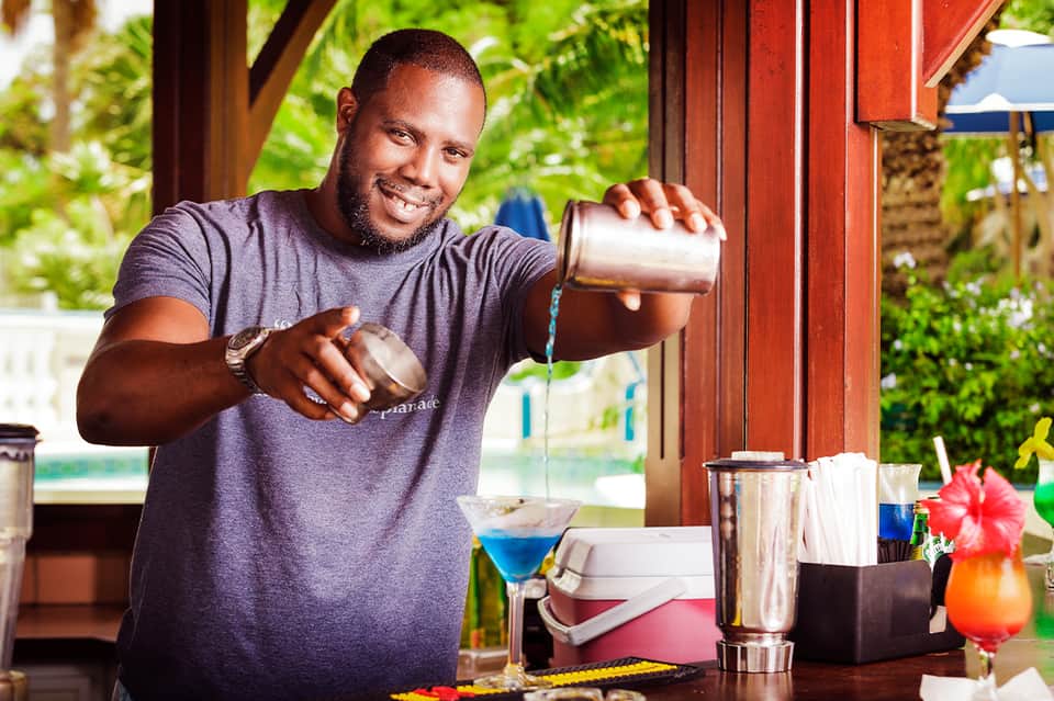 Bartender smiling while making a blue cocktail at outdoor tropical bar setting