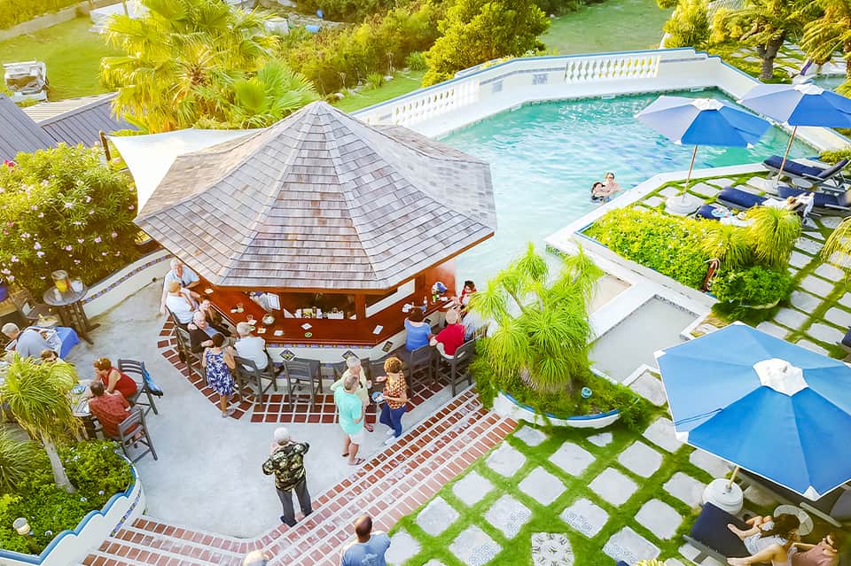 Aerial view of resort pool, wooden pavilion bar, and landscaped grounds with umbrellas