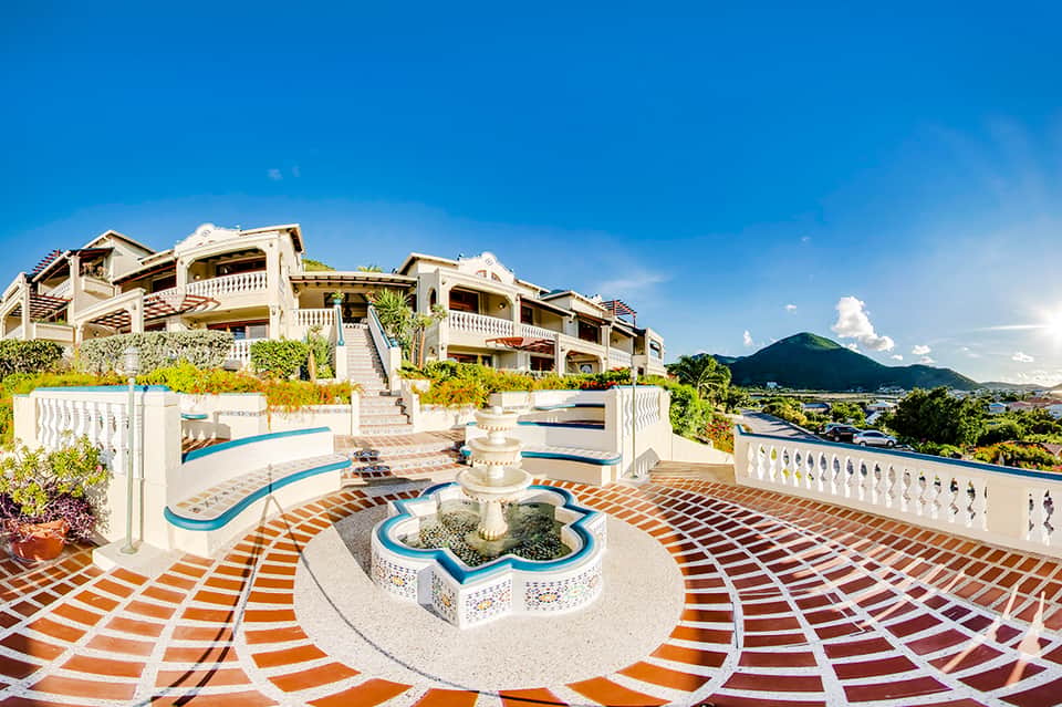 Luxury resort terrace with curved pools, white balustrades, colorful tiling, and mountain views