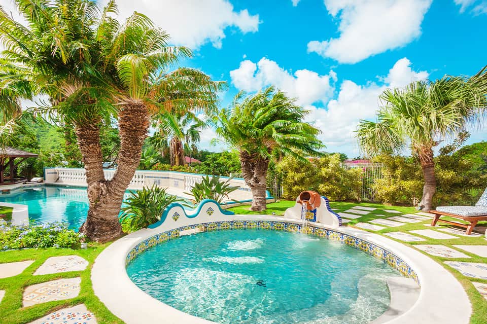 Resort pool area surrounded by palm trees, spa pools, and manicured green landscape