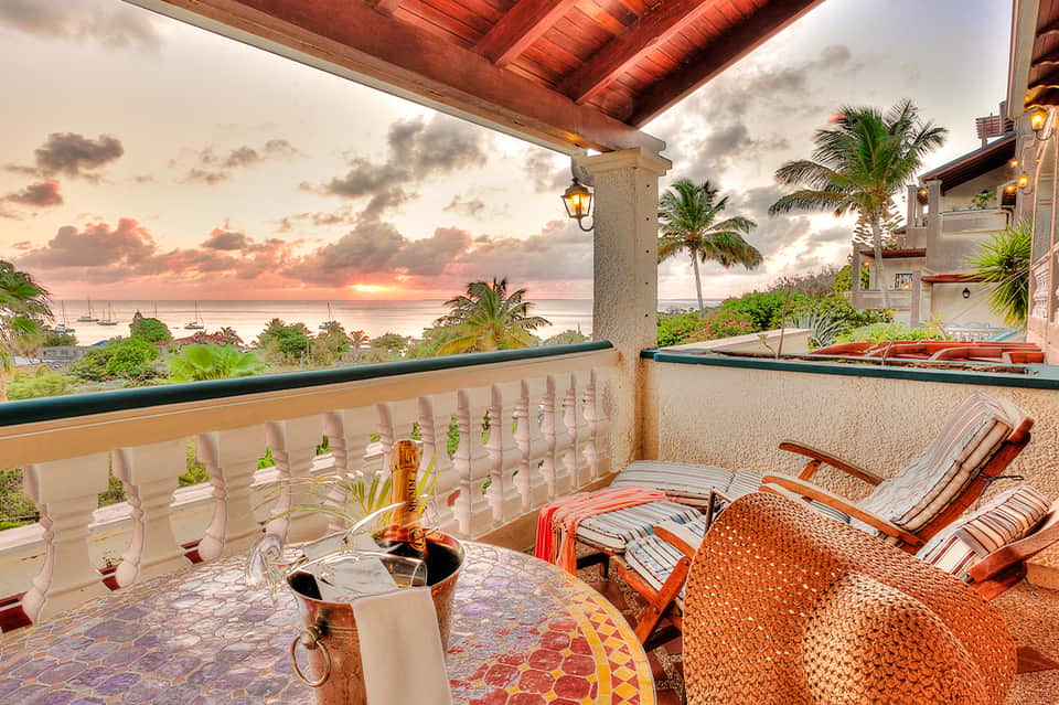 Sunset view from oceanfront resort balcony with palm trees and sailboats on horizon
