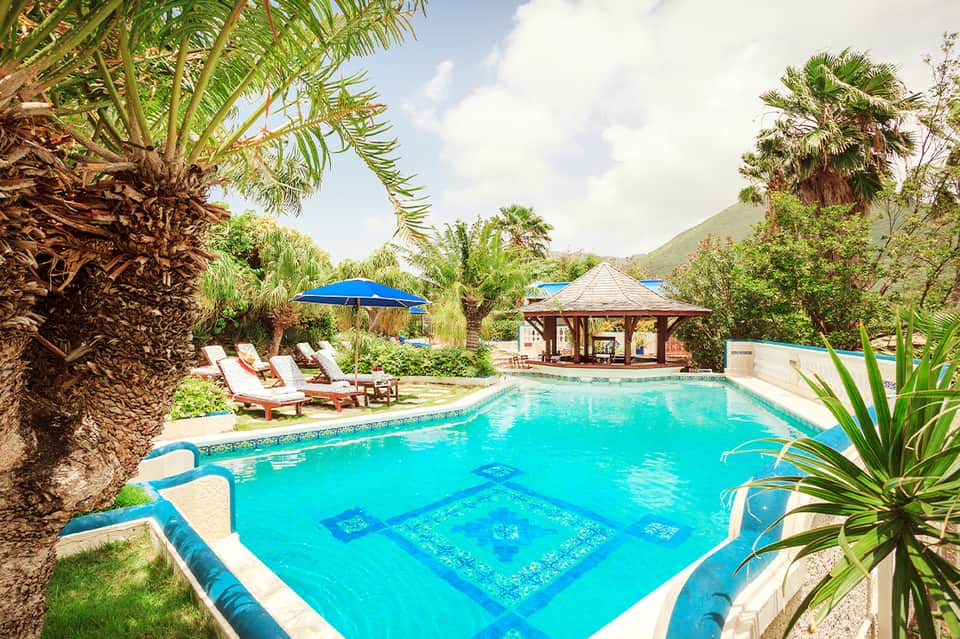 Resort pool surrounded by palm trees, blue umbrellas, lounge chairs, and gazebo structure