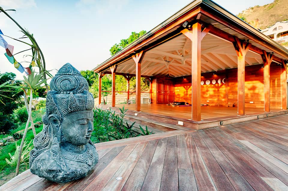 Balinese-style wooden pavilion with stone statue and tropical landscaping on hillside