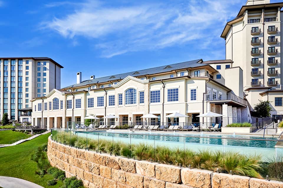 Exterior view of luxury hotel with resort pool, lawn seating, and multi-story buildings