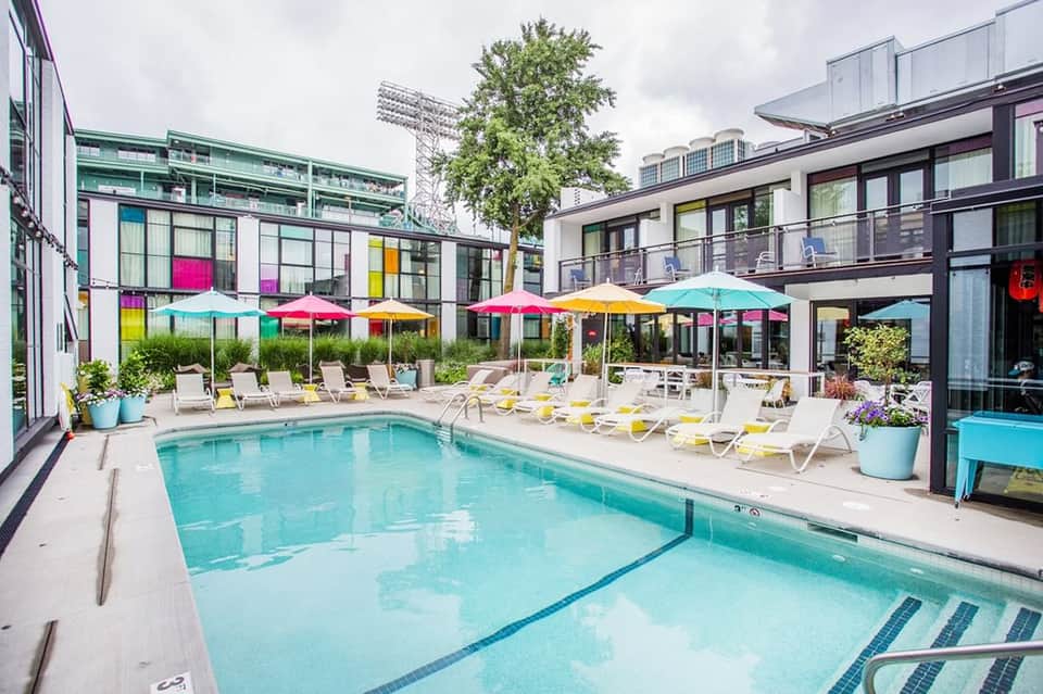 Contemporary pool area with colorful umbrellas, modern buildings, and lounge chairs