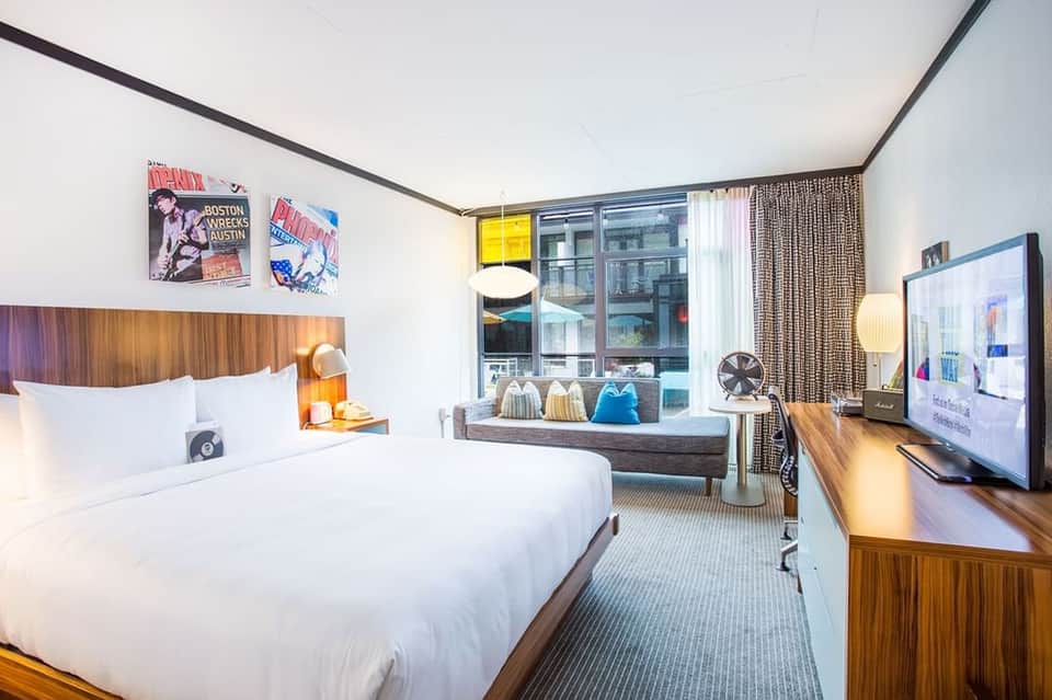 Modern hotel bedroom with wooden headboard, city views, and contemporary furnishings