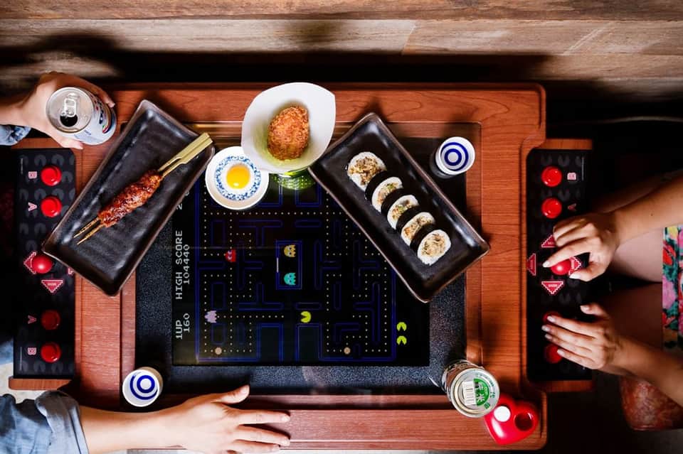 Overhead view of interactive gaming table with sushi and food surrounded by red game controllers