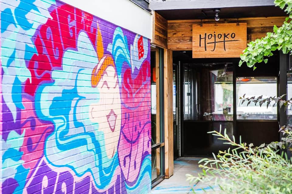 Colorful abstract street mural next to wooden storefront entrance with Hojoko signage