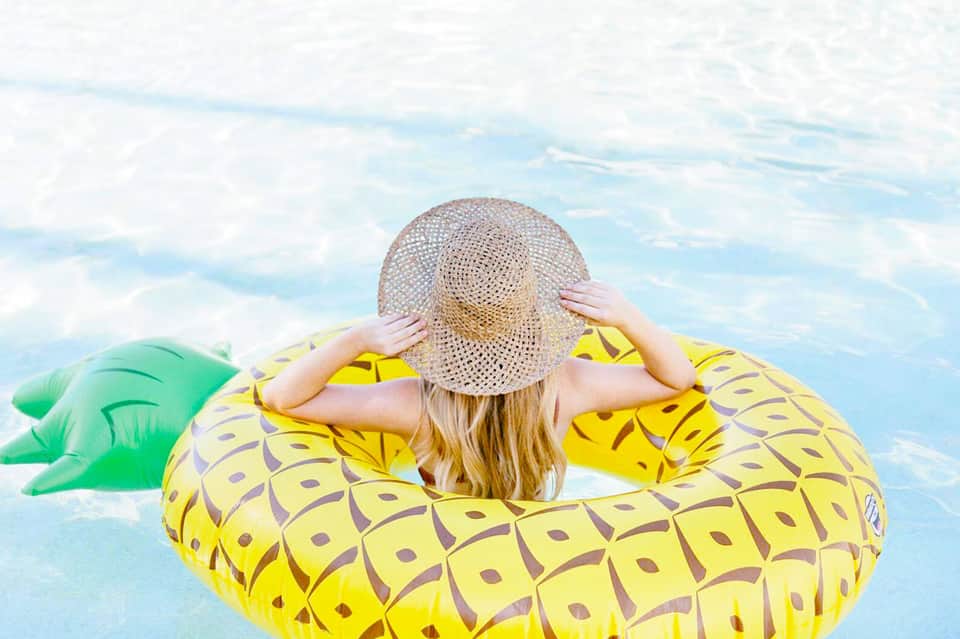 Woman in straw hat floating on yellow pineapple pool float in blue water