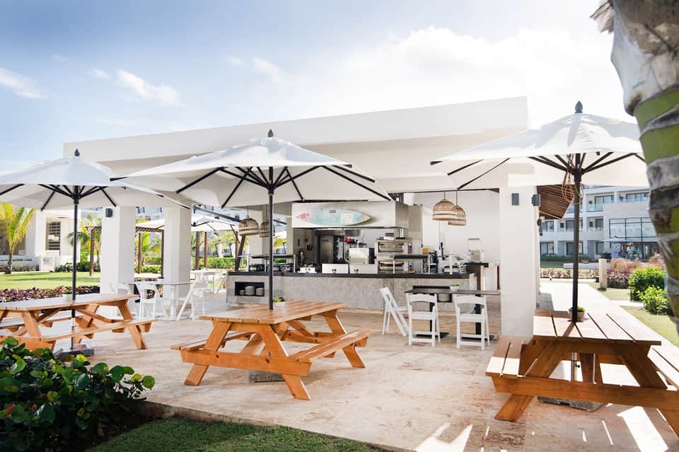 Beachfront restaurant pavilion with white umbrellas, picnic tables, and open-air kitchen