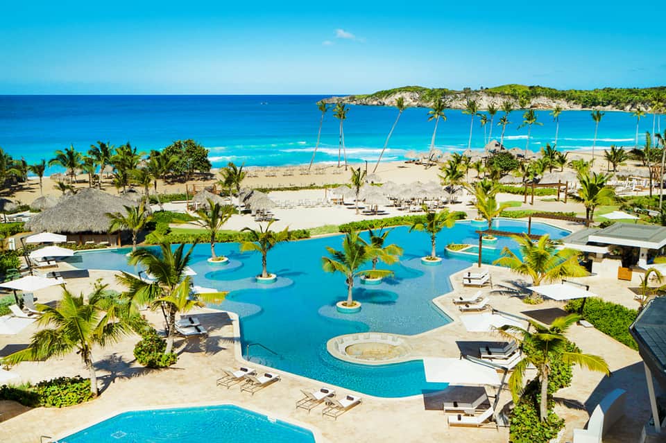 Large resort pool with palm trees and beach view in background