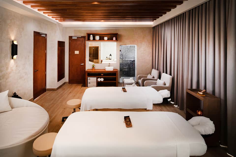 Spa treatment room with two massage tables, wooden ceiling beams, and modern amenities