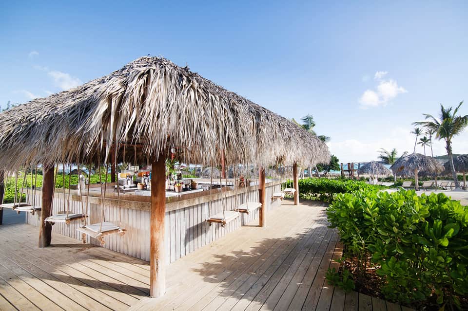 Beachfront tiki bar with thatched roof and wooden railings near palm trees