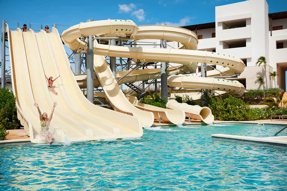 Water park with multiple tall cream-colored slide towers and children splashing in pool