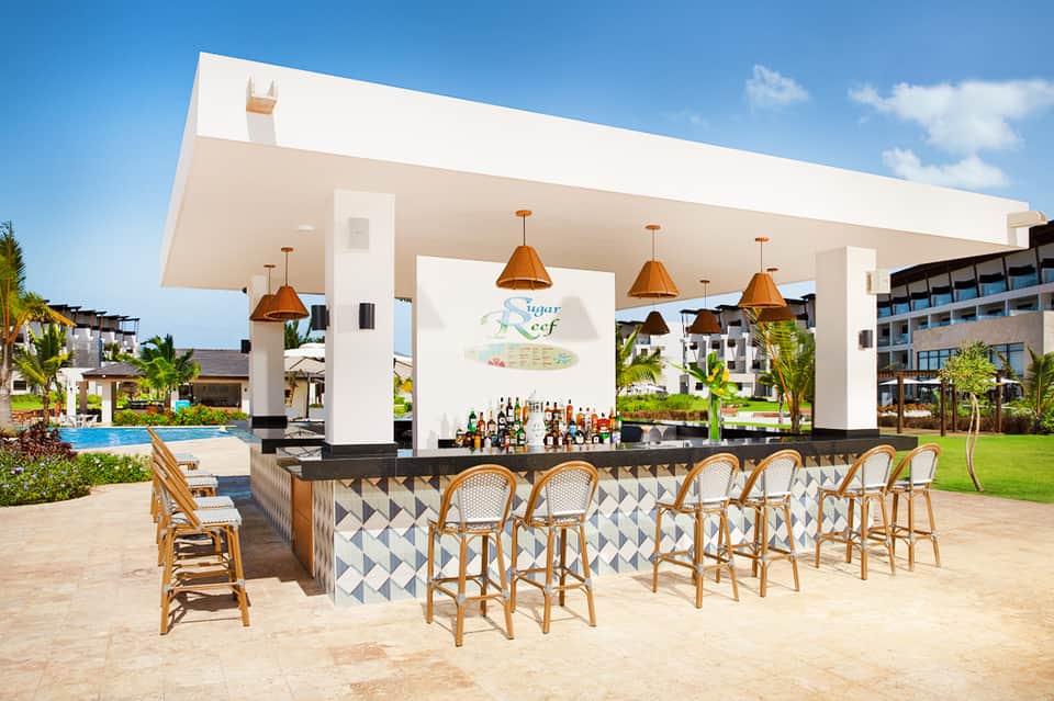 Contemporary beachfront bar with copper pendant lights, geometric tile patterns, and tropical landscaping