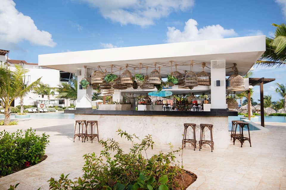 Open-air beachfront bar with white canopy and hanging basket lights overlooking pool