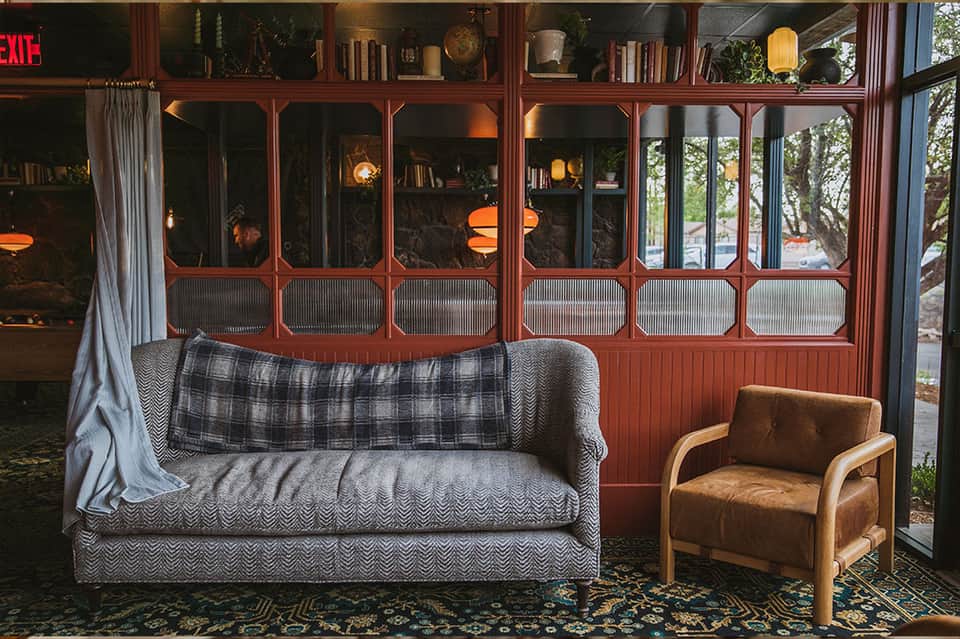 Vintage-style living room with gray patterned sofa, plaid throw, tan chair, and red-framed windows